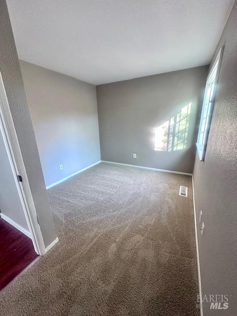 unfurnished room with a textured ceiling, carpet flooring, visible vents, and baseboards