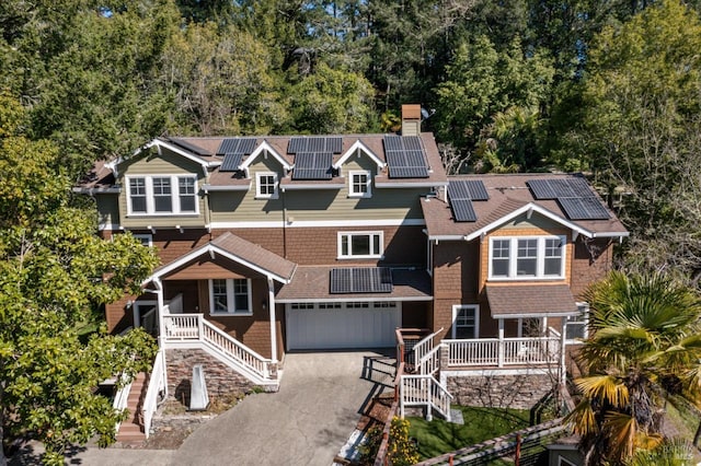 view of front of home with a chimney, aphalt driveway, an attached garage, covered porch, and roof mounted solar panels