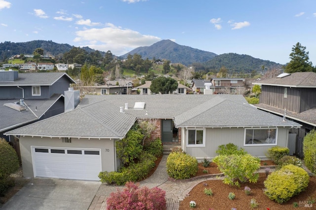 exterior space featuring driveway, a shingled roof, an attached garage, and a mountain view