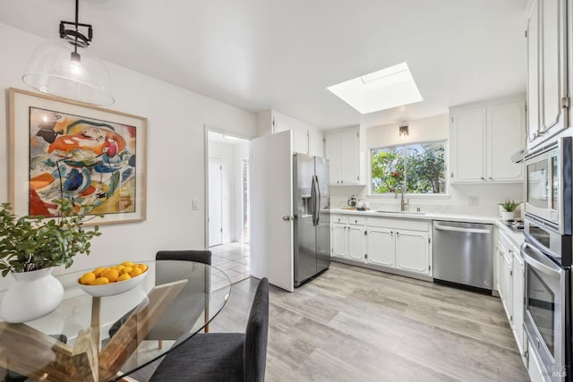 kitchen with a skylight, appliances with stainless steel finishes, light countertops, white cabinetry, and a sink