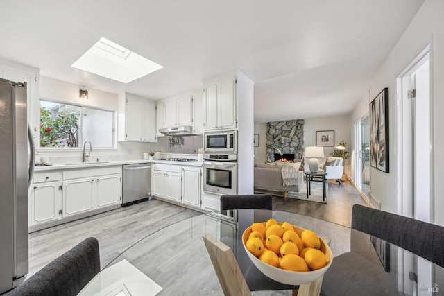 kitchen with a skylight, stainless steel appliances, a sink, a stone fireplace, and under cabinet range hood