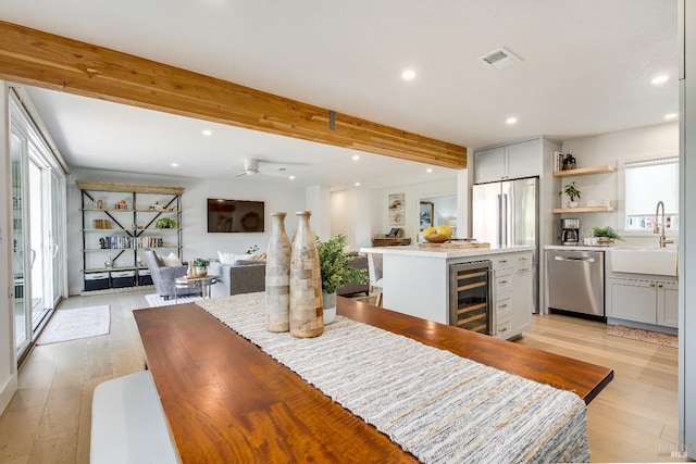 dining area featuring a healthy amount of sunlight, wine cooler, visible vents, and beamed ceiling