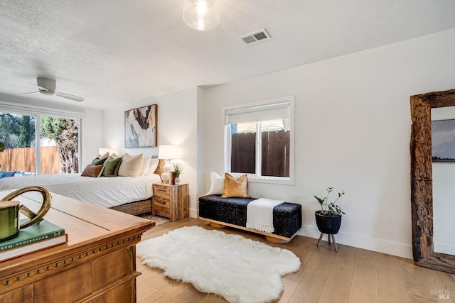 bedroom with baseboards, light wood-style flooring, visible vents, and a textured ceiling