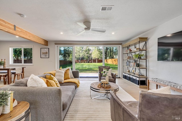 living area with visible vents, a ceiling fan, a textured ceiling, light wood-type flooring, and beamed ceiling