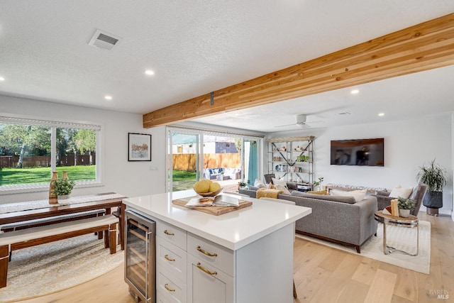 kitchen with a center island, light wood finished floors, light countertops, visible vents, and beverage cooler