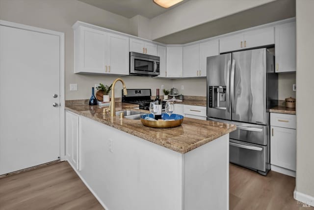 kitchen featuring light wood finished floors, a peninsula, light stone countertops, stainless steel appliances, and white cabinetry