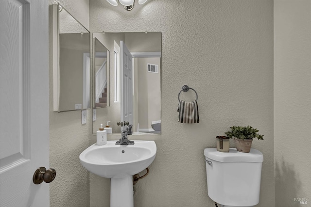 half bathroom featuring visible vents, toilet, and a textured wall