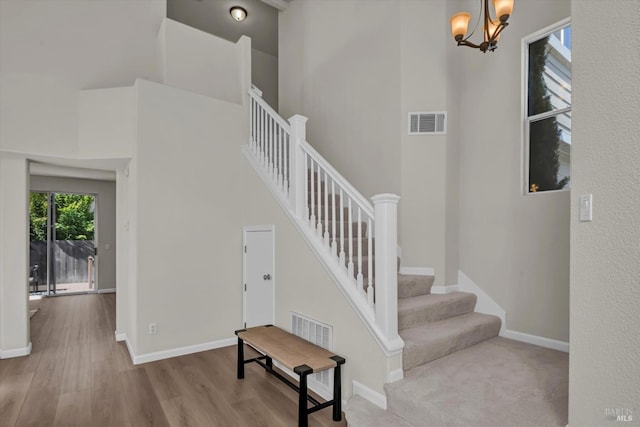 staircase featuring a towering ceiling, wood finished floors, visible vents, and baseboards