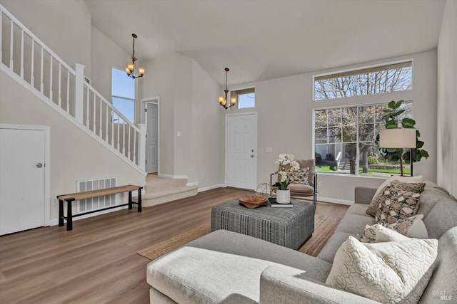 living room featuring visible vents, stairway, wood finished floors, an inviting chandelier, and high vaulted ceiling