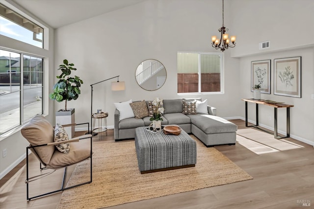 living room featuring baseboards, a chandelier, a high ceiling, visible vents, and wood finished floors