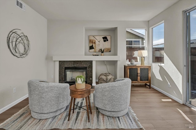 living area featuring wood finished floors, a glass covered fireplace, visible vents, and baseboards