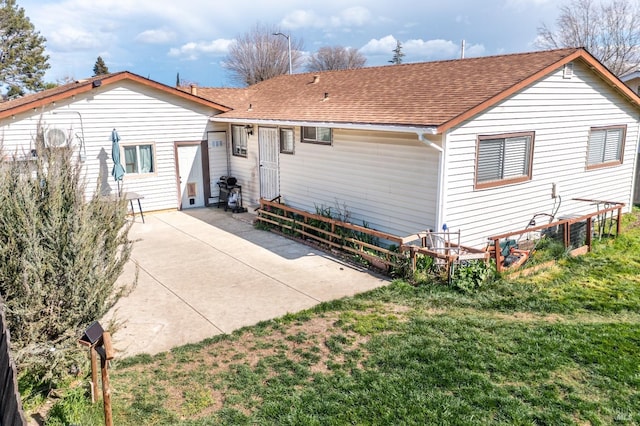 rear view of property featuring a patio, a lawn, and roof with shingles