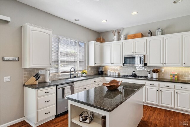 kitchen with white cabinetry, dark wood-type flooring, dark stone counters, a sink, and appliances with stainless steel finishes
