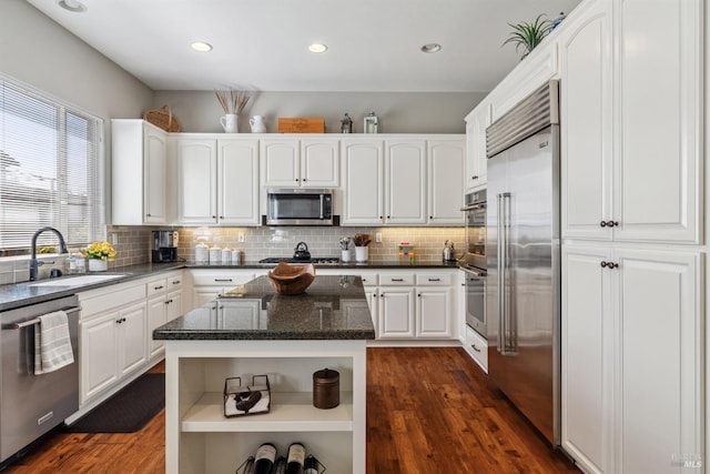 kitchen with white cabinets, stainless steel appliances, a sink, open shelves, and backsplash