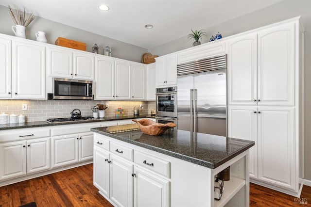 kitchen with backsplash, appliances with stainless steel finishes, dark wood finished floors, white cabinets, and dark stone counters
