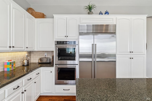 kitchen with white cabinetry, dark stone counters, stainless steel appliances, and backsplash