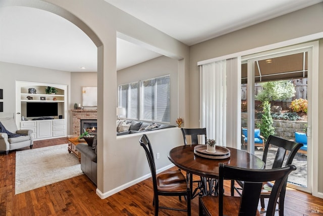 dining room with built in shelves, a fireplace, wood finished floors, baseboards, and arched walkways