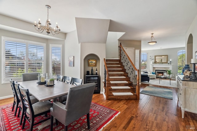 dining area with baseboards, stairway, a glass covered fireplace, a notable chandelier, and wood-type flooring