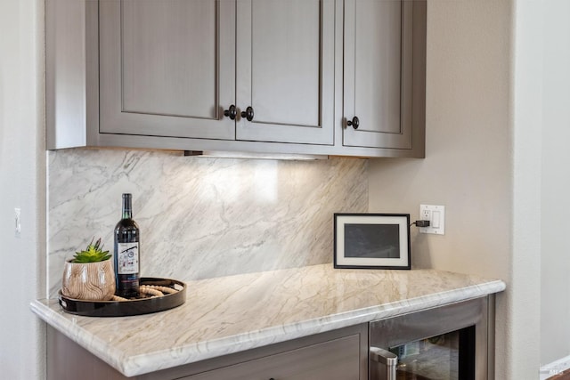 kitchen featuring tasteful backsplash, wine cooler, gray cabinetry, and light stone counters