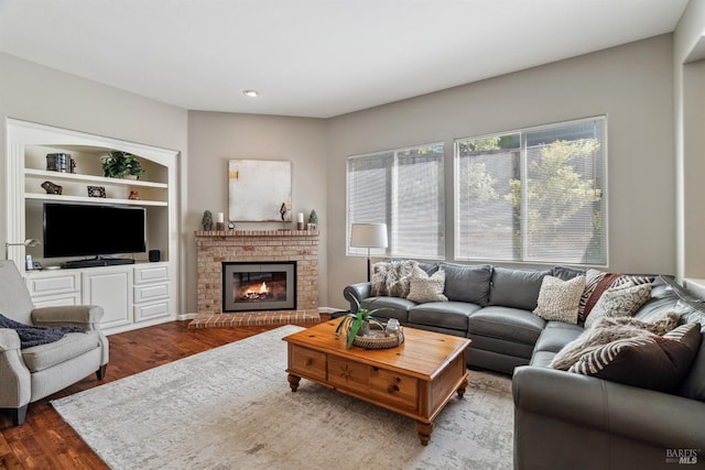 living room featuring a brick fireplace, recessed lighting, built in shelves, and wood finished floors