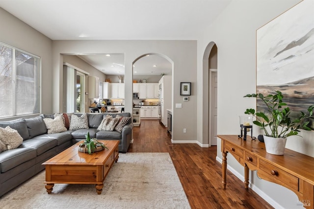 living room with arched walkways, dark wood-type flooring, baseboards, and recessed lighting