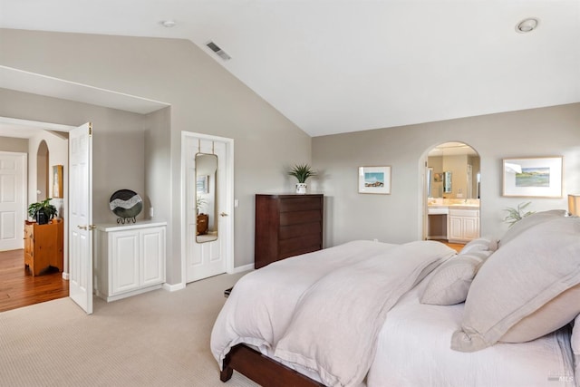 bedroom with arched walkways, lofted ceiling, connected bathroom, and visible vents