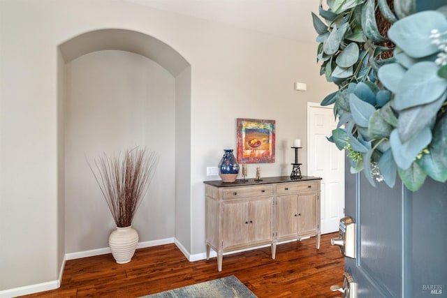 hallway with arched walkways, dark wood-style floors, and baseboards