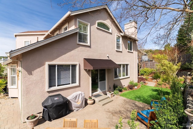 rear view of property featuring a chimney, stucco siding, fence, and a patio area