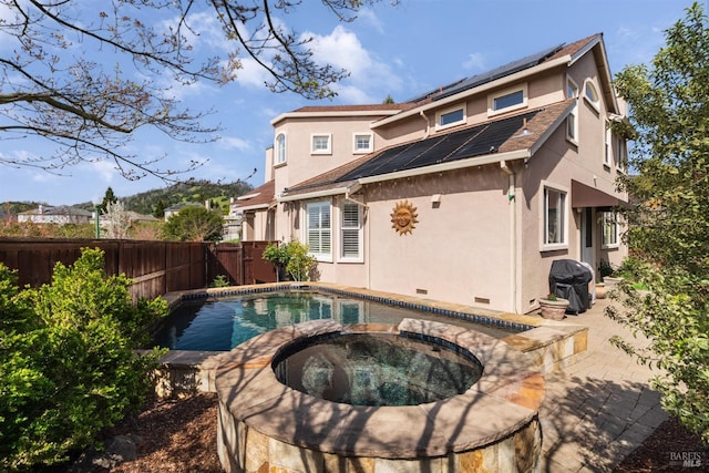 rear view of property with stucco siding, a patio, a fenced backyard, an in ground hot tub, and roof mounted solar panels