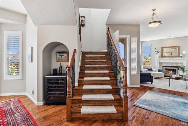 stairs with baseboards, wine cooler, arched walkways, a glass covered fireplace, and wood finished floors