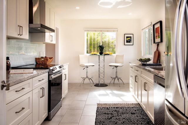 kitchen with stainless steel appliances, backsplash, white cabinets, light stone countertops, and wall chimney exhaust hood