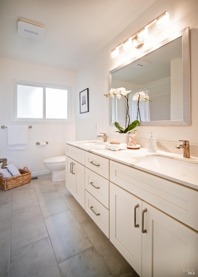 bathroom featuring toilet, double vanity, and a sink