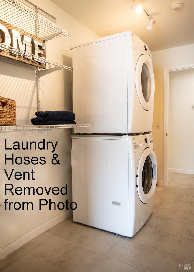 laundry area featuring laundry area, track lighting, stacked washer and clothes dryer, and baseboards