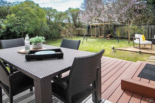 wooden deck featuring outdoor dining space, a fenced backyard, a lawn, and a playground