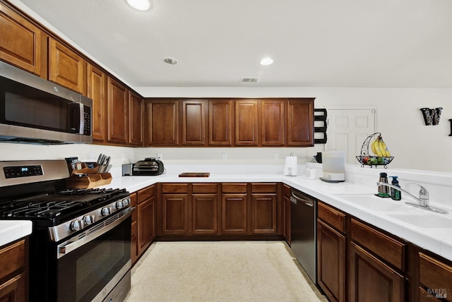 kitchen featuring recessed lighting, stainless steel appliances, a sink, light countertops, and light floors