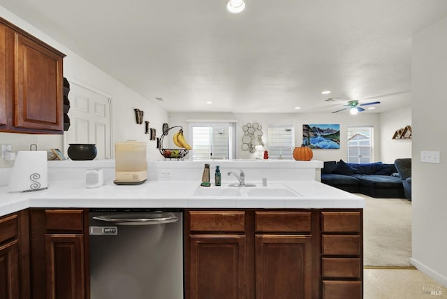 kitchen featuring a peninsula, a sink, open floor plan, stainless steel dishwasher, and tile counters