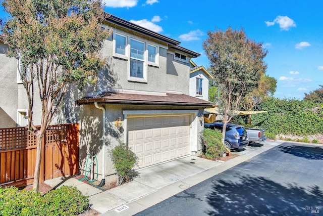 view of front of home with a garage, concrete driveway, fence, and stucco siding