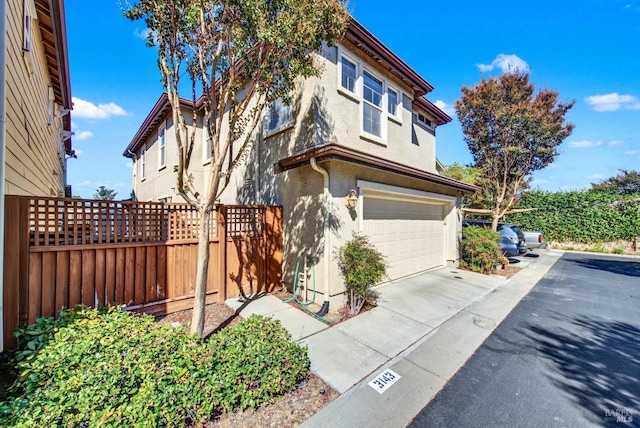 view of front of property with a garage, driveway, fence, and stucco siding