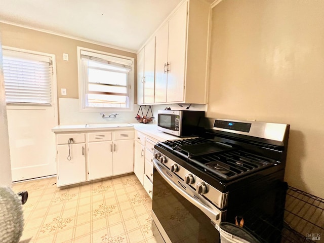 kitchen featuring light floors, light countertops, appliances with stainless steel finishes, white cabinetry, and a sink