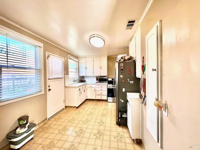 kitchen featuring light floors, stainless steel appliances, visible vents, white cabinets, and a sink