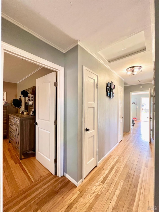 hallway with ornamental molding, light wood-style flooring, and baseboards