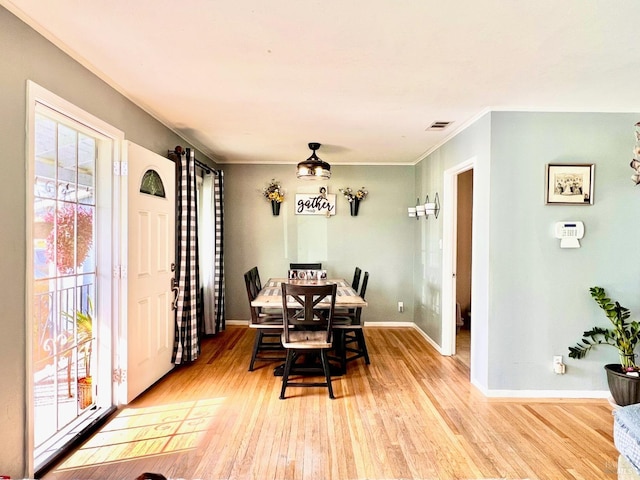 dining space featuring light wood finished floors, visible vents, baseboards, and crown molding