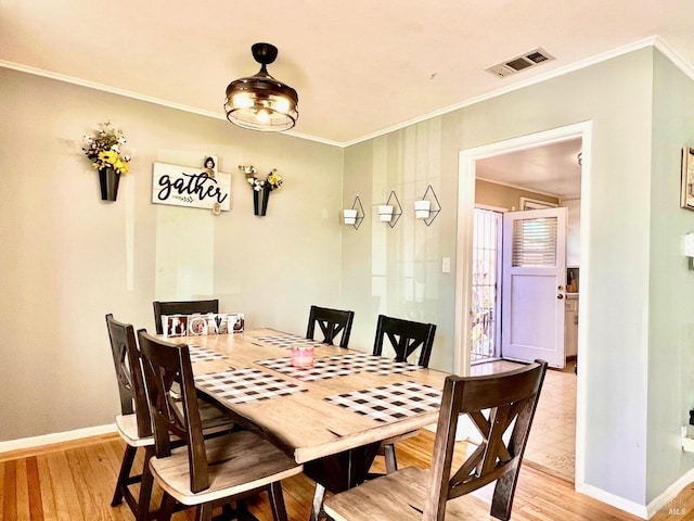 dining space featuring light wood-type flooring, visible vents, crown molding, and baseboards