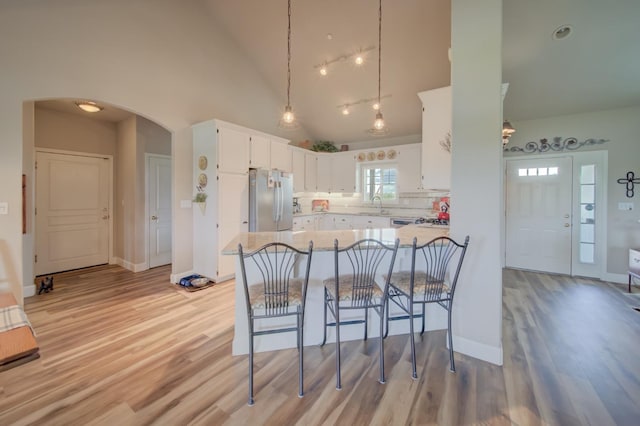kitchen featuring arched walkways, white cabinetry, a sink, light wood-style floors, and freestanding refrigerator