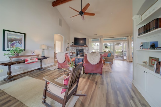 living area with a ceiling fan, a fireplace, wood finished floors, visible vents, and beamed ceiling