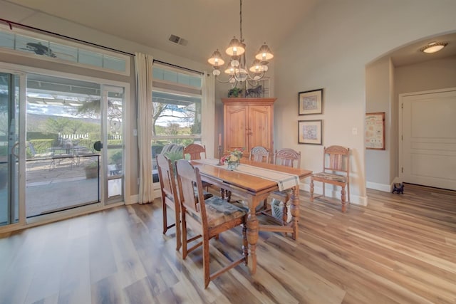 dining space with baseboards, arched walkways, light wood-style floors, visible vents, and a notable chandelier