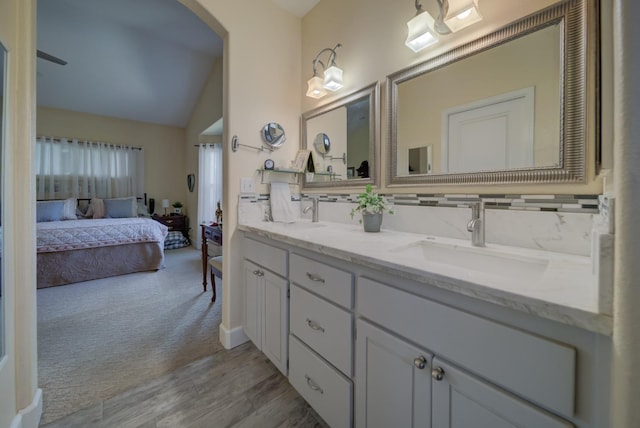 ensuite bathroom with double vanity, tasteful backsplash, lofted ceiling, a sink, and ensuite bath