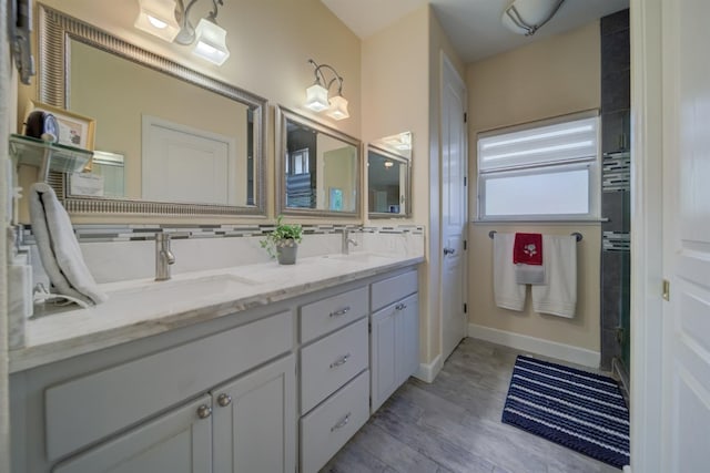 bathroom with a sink, backsplash, wood finished floors, baseboards, and double vanity