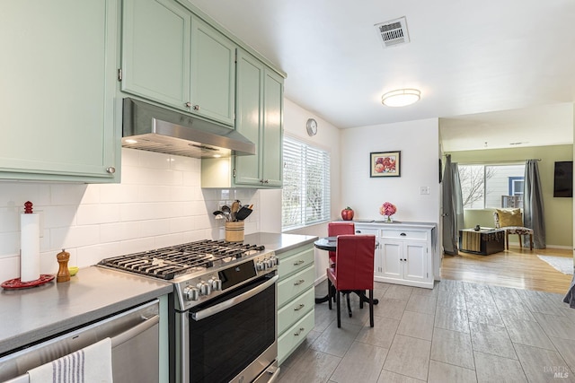 kitchen featuring stainless steel appliances, backsplash, green cabinetry, and under cabinet range hood