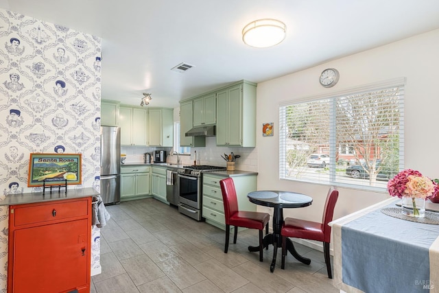 kitchen featuring under cabinet range hood, stainless steel appliances, visible vents, green cabinets, and decorative backsplash